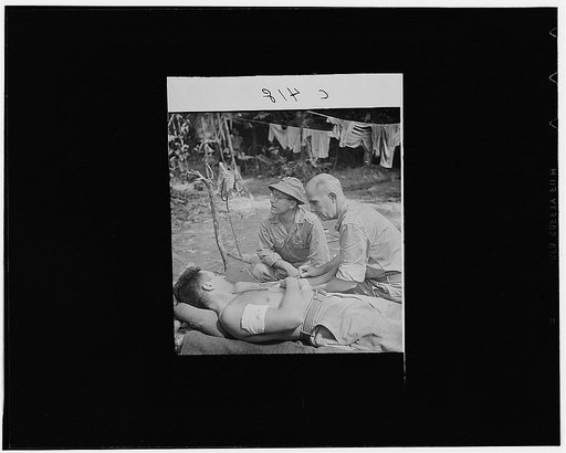 Buna, New Guinea. A wounded man behind the lines on the Buna front being given a blood transfusion. Lieutenant J.J. Gotow, of Flint, Michigan, is assisting Captain W.F. Edwards, of New Albany, Indiana