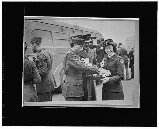 London England. Hope Simpson, from Montreal, offering American soldiers cigarettes and candy after they have taken part in the Allied nations' procession, a feature of London's "Wings for Victory" week celebration. Miss Simpson has been living in London for six years, but was in France when that nat