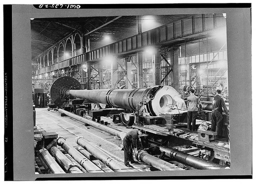 Scene in a gun plant where the big guns and shells are made, showing in the foreground a sixteen-inch naval gun being gauged after boring