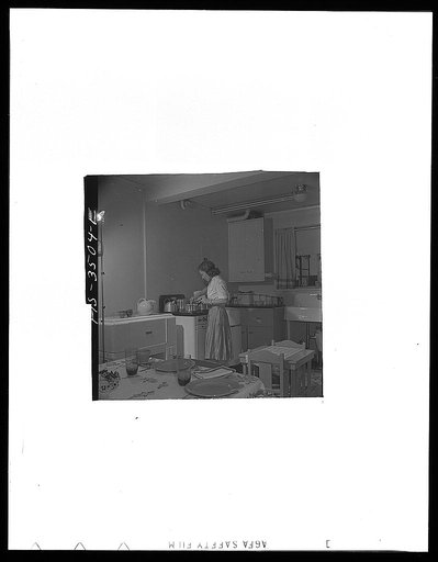Greenbelt, Maryland. Federal housing project. Mrs. Leslie Atkins preparing dinner in her kitchen, one end of which is the dining room. Notice the mangle and washing machine on either side of the stove