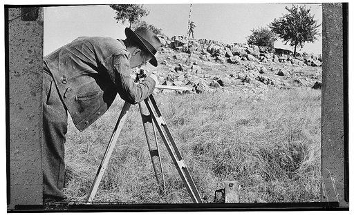 America's petroleum industries pour out fuel and lubricants for the United Nations. A geologist, employed by one of the important U.S. oil companies, surveys, with the help of his "rod man" standing on the ridge in the background, a section of land to detect the presence of a possible oil deposit un