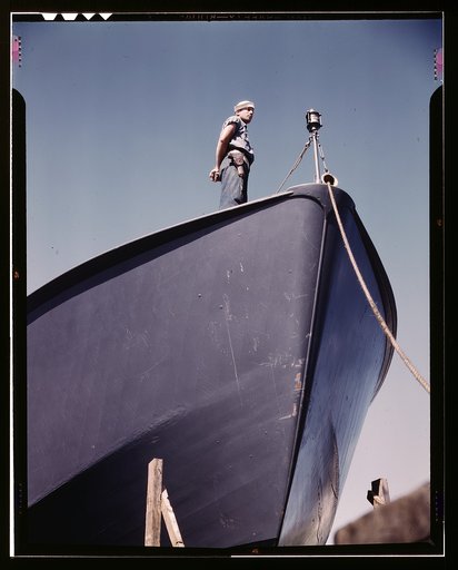 A Coast Guard sentry stands watch over a new torpedo boat under construction at a southern shipyard. In addition to wooden torpedo boats, the yard also turns out many steel boats for the Navy. Higgins Industries, Inc., New Orleans, La.