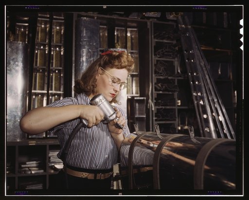 Operating a hand drill at North American Aviation, Inc., [a] woman is working in the control surface department assembling a section of the leading edge for the horizontal stabilizer of a plane, Inglewood, Calif.