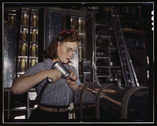 Operating a hand drill at the North American Aviation, Inc., [a] woman is in the control surface department assembling a section of the leading edge for the horizontal stabilizer of a plane