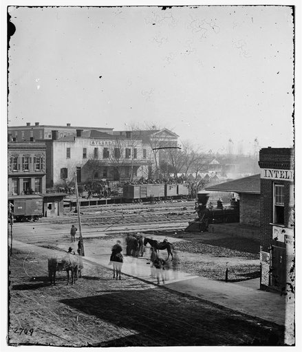 Atlanta, Ga. Civilians crowded on tops of boxcars at railroad depot as soldiers gather around an S.D. Goodale & Sons stereoscopic viewer next to office of the Daily Intelligencer newspaper