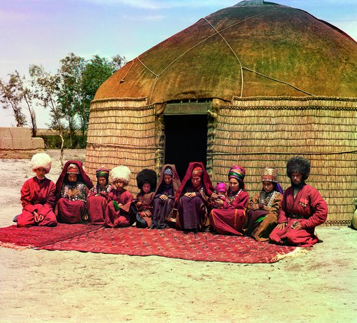Group of eleven adults and children, seated on a rug, in front of a yurt