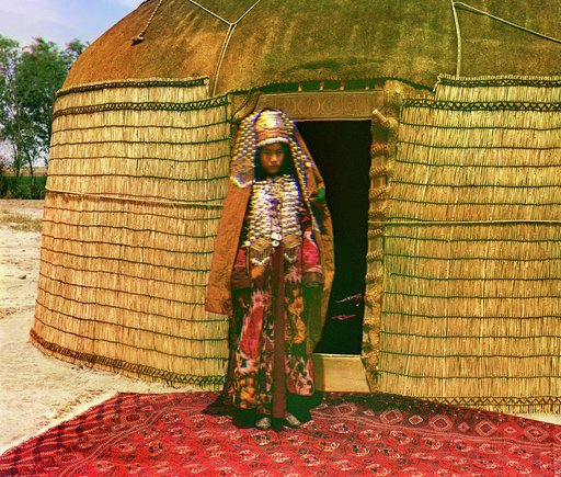 Woman in traditional dress and jewelry standing on rug in front of yurt