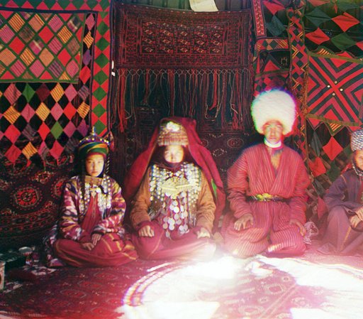 Four people seated on a carpet, in front of a backdrop of textiles