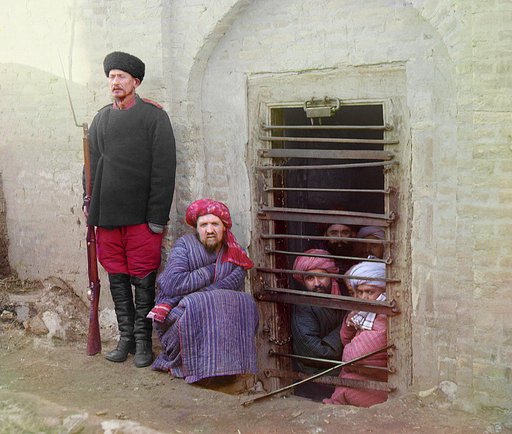 Zindan (prison), with inmates looking out through the bars and a guard with Russian rifle, uniform, and boots, Central Asia