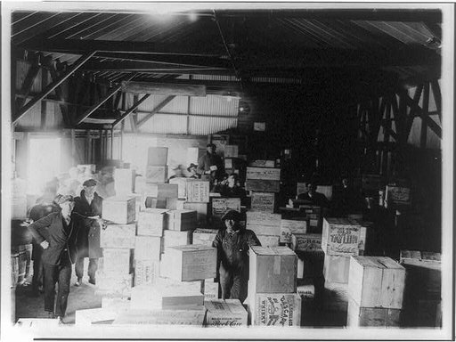 Men standing in warehouse with cases of confiscated(?) liquor