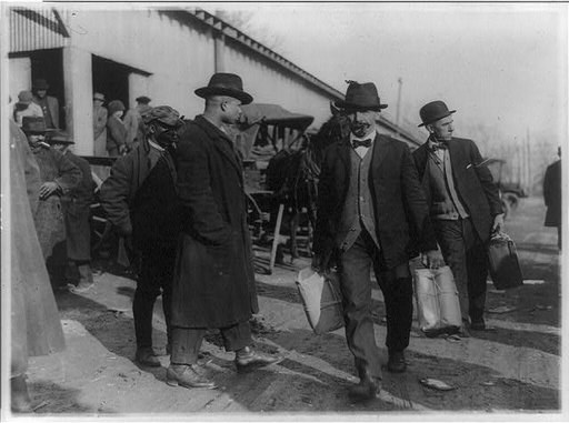 Two men of the U.S. Internal Revenue Bureau(?) carrying packages of confiscated liquor(?) past two black men