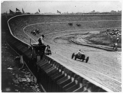 Automobile racing on curved wood track, probably in or near Washington, D.C., with flag man in foreground