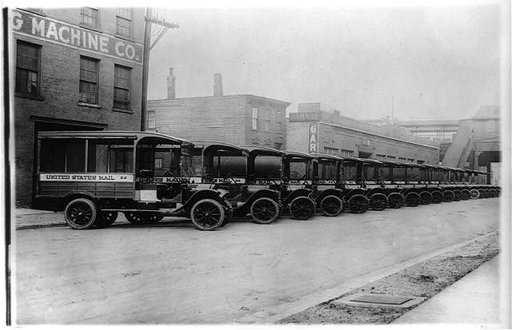 Mail trucks parked in a row in front of commercial buildings