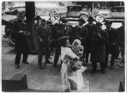News photographers photographing Paulina Longworth, daughter of Nick and Alice Longworth, being held by woman on sidewalk, Washington, D.C.