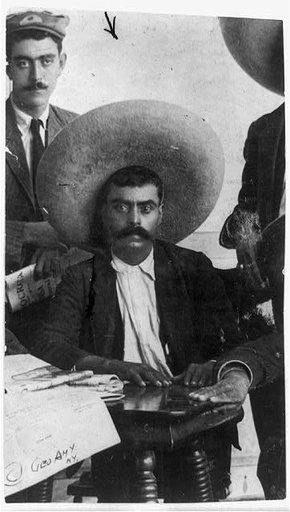 Emiliano Zapata, three-quarter length portrait, facing front, seated at table between two standing men