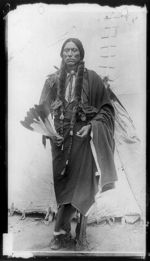 Quanah Parker, Comanche Indian Chief, full-length portrait, standing, facing front, holding feathers, in front of tepee