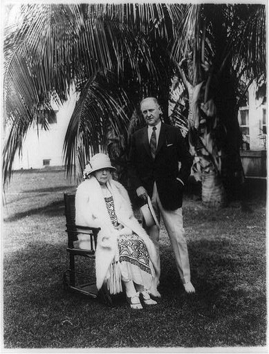 Atty. Gen. Harry Micajah Daugherty, full-length portrait, standing next to wife, under palm tree