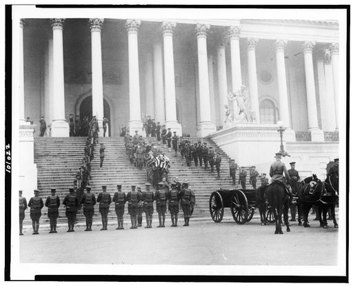Coffin of the Unknown Soldier being brought down steps of the U.S. Capitol, where horse-drawn wagon awaits; military personnal stand at attention