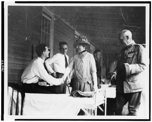 Mrs. Warren G. Harding shaking hands with man seated on bed in military barracks(?)