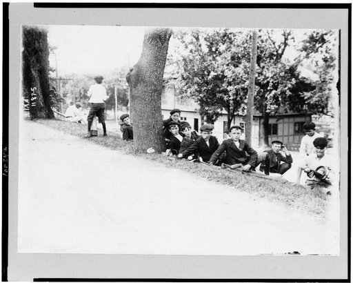 Group of boys with golf clubs--probably caddies--resting on hill