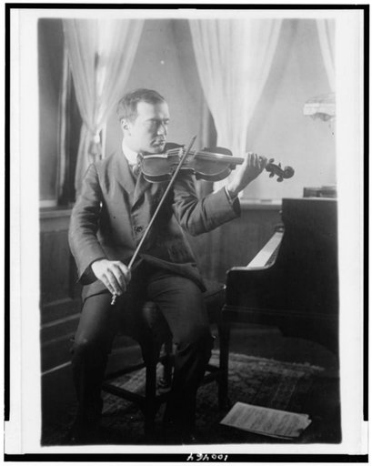 Bronislaw Huberman, full-length portrait, seated, facing right, playing violin