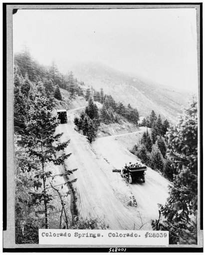 Colorado Springs, Colorado. Two automobiles going down mountain road, with horseshoe turn in foreground