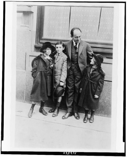 Ernest Bloch, full-length portrait, standing, facing right, with three children