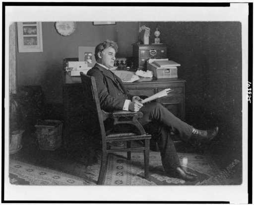 David Belasco, full-length portrait, seated at desk, facing right