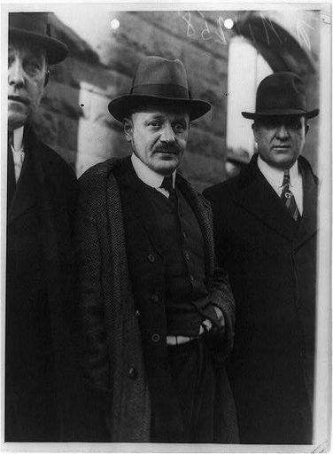 Hans Schwartz, three-quarter length portrait, standing, facing slightly right, with two detectives on way to court, New Jersey