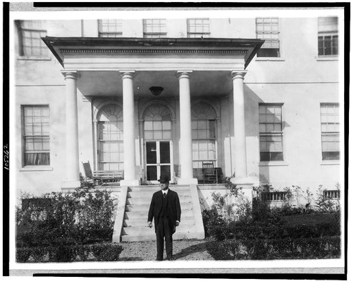 Hiram W. Johnson, full-length portrait, standing outside of mansion, facing left