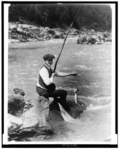 Man seated on rock, with two fish on line, by stream, possibly the River, Washington, D.C. area