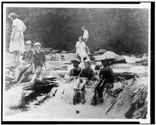 Three boys seated in creek, and three girls and two boys on rocks in Rock Creek, Washington, D.C.
