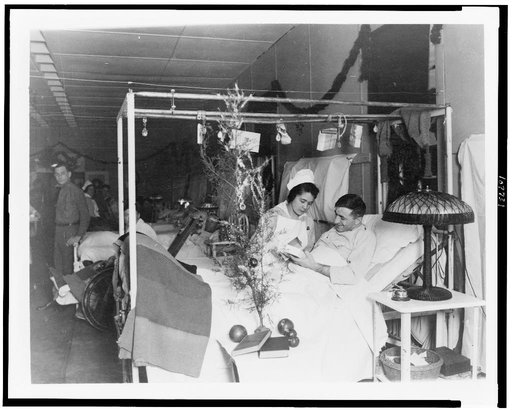 Red Cross nurse alongside of soldier in hospital bed, with Christmas decorations