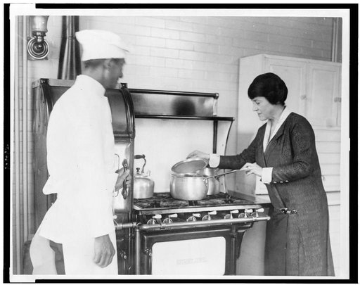 Mary Roberts Rinehart, lifting lid of pot on stove, and chef standing alongside