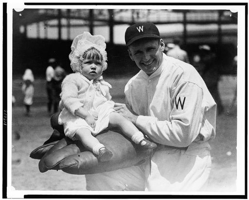 Walter Johnson, half-length portrait, facing slightly left, holding little girl on large glove