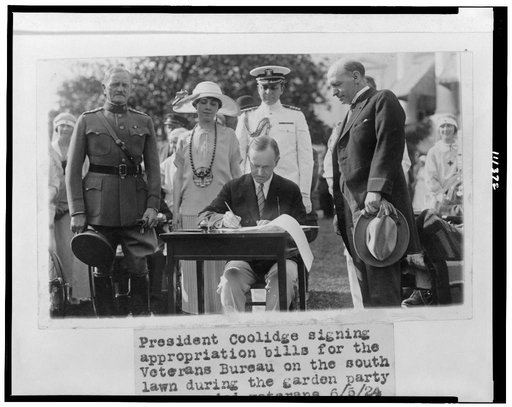 President Coolidge signing appropriation bills for the Veterans Bureau on the south lawn during the garden party for wounded veterans