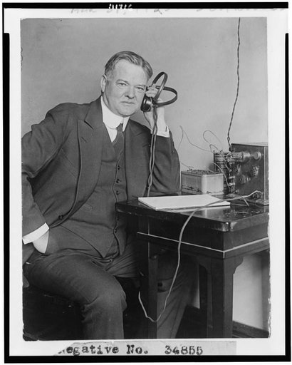 Herbert Hoover, three-quarter length portrait, seated, facing slightly right, listening to radio