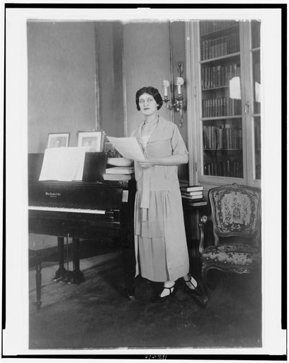 Alma Gluck, full-length portrait, standing by piano, facing slightly left