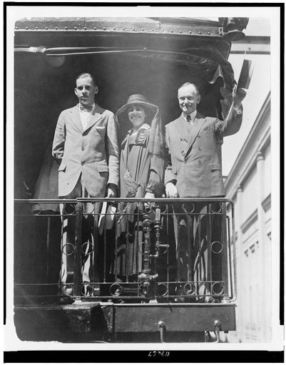 President Calvin Coolidge, full-length portrait, standing, facing slightly left, with wife and son, on back of railroad train