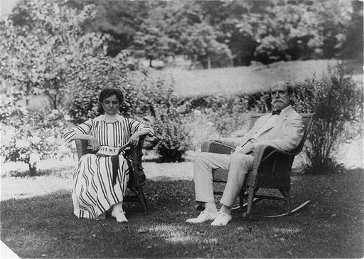 Charles Evans Hughes, full-length portrait, seated in rocker on lawn, facing left, with wife