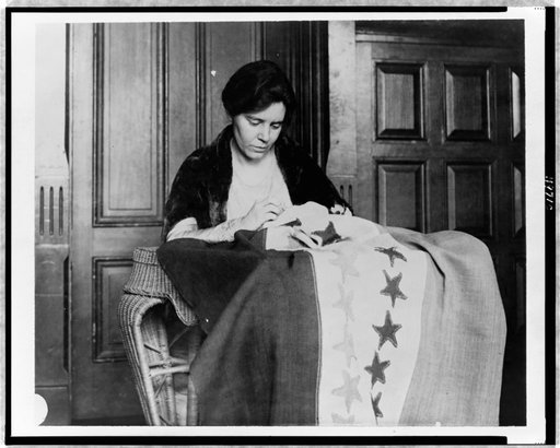 Alice Paul, half-length portrait, seated, facing slightly right, sewing suffrage flag