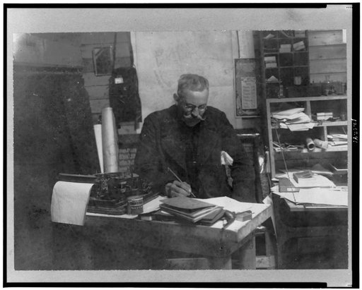 Walter Wellman, half-length portrait, seated at desk, facing slightly right, with pen in hand, looking downward, Spitzbergen