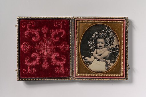 [Smiling, Nude Baby Holding Foot, Seated on Furniture Draped with Floral Print Fabric]