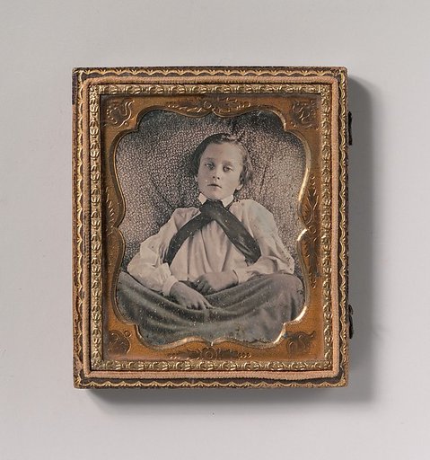 [Boy Seated Cross-legged, Partially Covered by Blanket, Leaning Against Cushion]