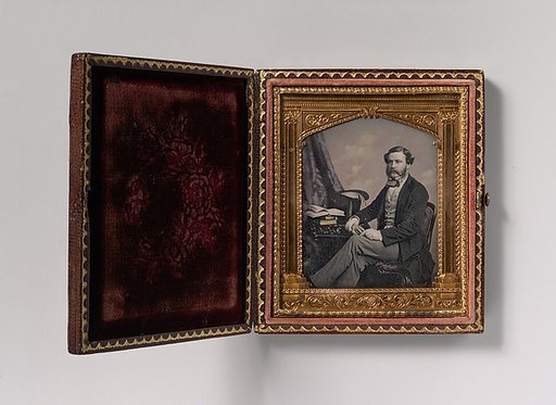 [Man Seated in Front of Cloud Backdrop, Books and Top Hat on Table]