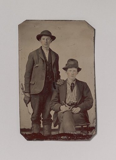 [Two Young Men, One Seated and One Standing, Holding Carpentry Tools]