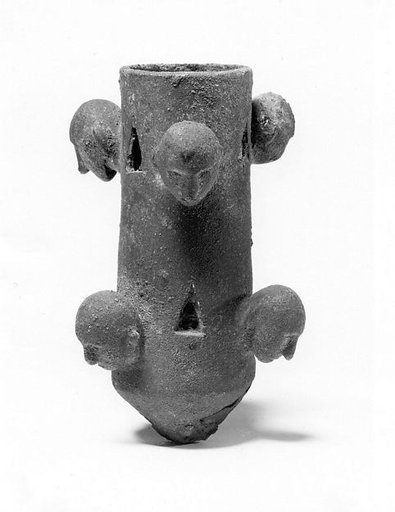 Tubular object with projecting human heads and triangular cut-outs