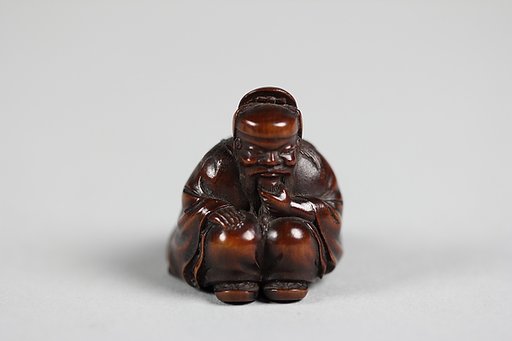Netsuke of Seated Figure of an Old Man with Backpack Containing a Mask