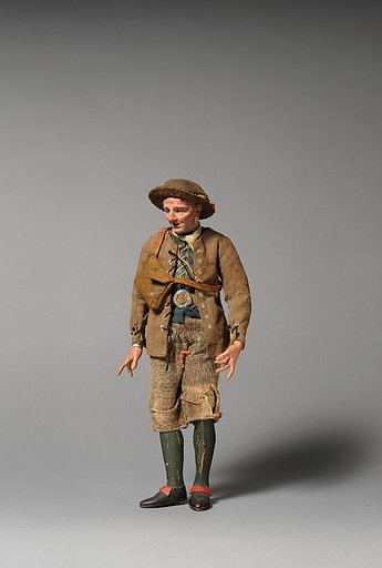 Man in brimmed hat, brown lace-up jacket, green vest, belt buckle, shoulder bag
