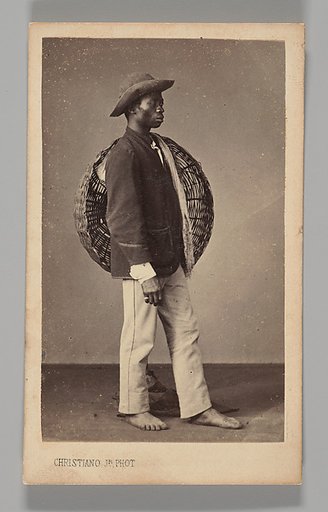 [Studio Portrait: Male Street Vendor Standing in Profile Holding Basket, Brazil]